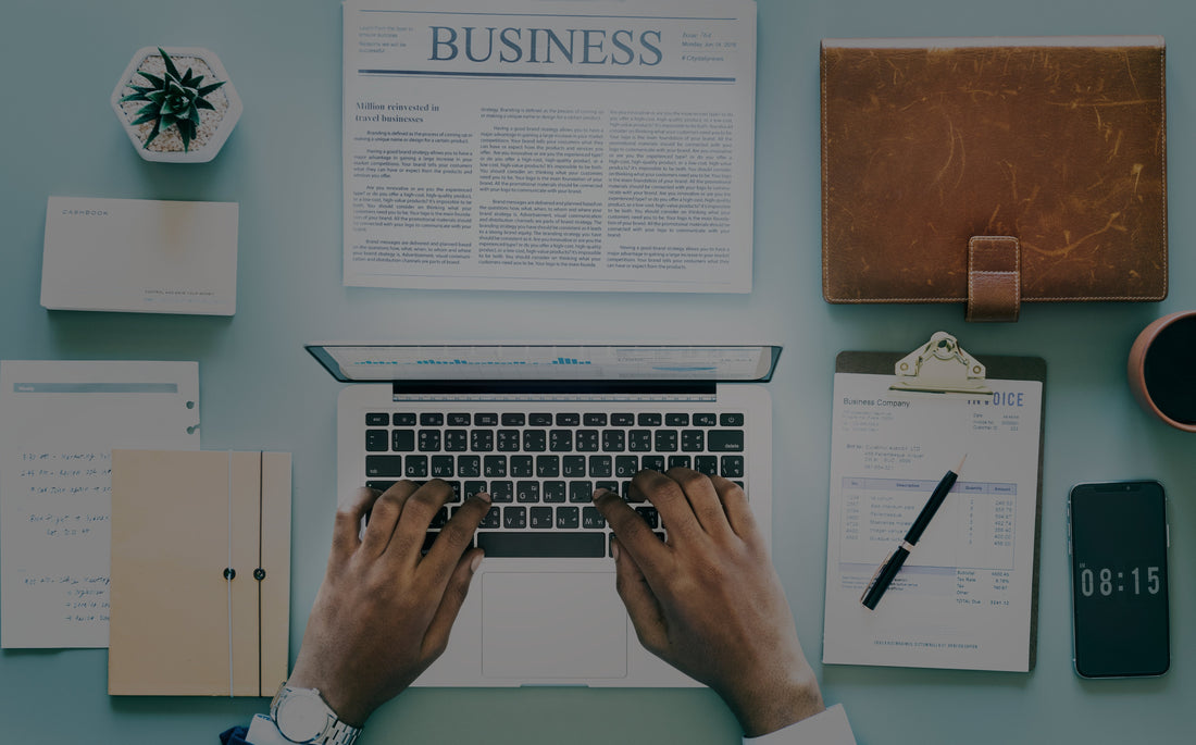 Overhead view of a person typing on a laptop surrounded by business documents and a smartphone.